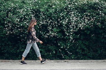 hipster woman in sunglasses walking on background of blooming bush with white flowers of spirea....