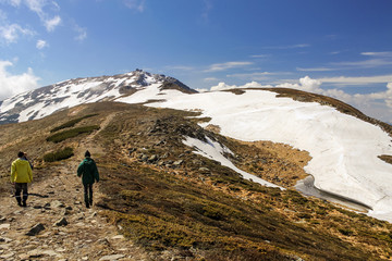Fototapeta premium men hikers walking on mountain valley road way to the abandoned observatory during spring snow covering the hills