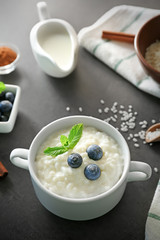 Delicious rice pudding in soup bowl with blueberries and mint leaves on kitchen table
