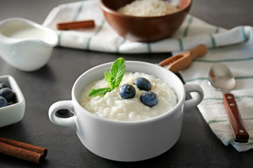 Delicious rice pudding in soup bowl with blueberries and mint leaves on kitchen table