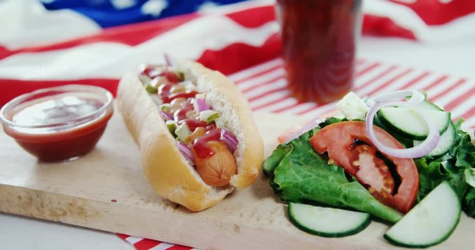 Hot dog, sauce and salad served on wooden board