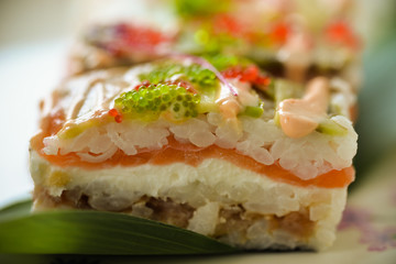 Macro pressed roll with salmon, cream cheese, tuna, avocado, tobiko and spicy sauce. Japanese fish food on blurred background. Nice photo for menu, cafe, restaurant, interior, design, posters, prints.