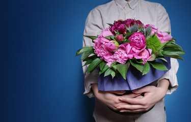 Young woman holding bucket with beautiful peonies on color background