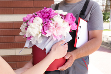 Young woman receiving beautiful peony flowers from delivery man