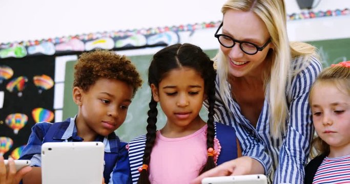 Teacher assisting schoolkid on digital tablet in classroom
