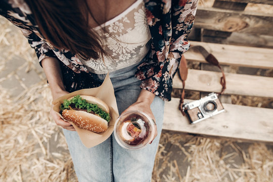 juicy burger and lemonade in hands, top view. stylish hipster woman holding  cheeseburger and refreshing drink. boho girl at street food festival. summer vacation picnic. space for text