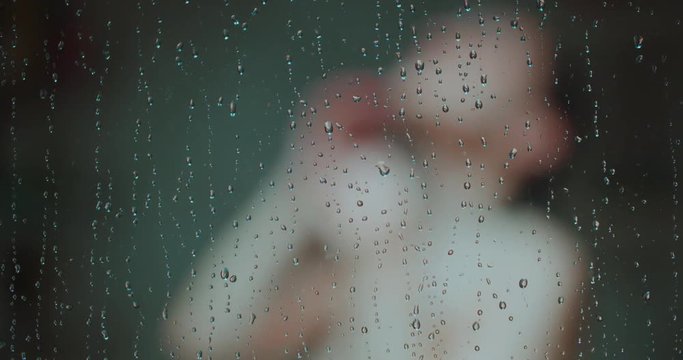 Woman Showering Focus on Water Drops on Door Move Right. a woman from chest up is blurred showering and turning while shot moves right focus on water drops on glass door falling in slow motion
