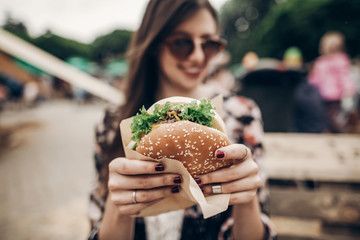 tasty burger. stylish hipster woman holding juicy hamburger in hands close up. boho girl with hamburger at street food festival. summertime. summer vacation picnic. space for text - obrazy, fototapety, plakaty