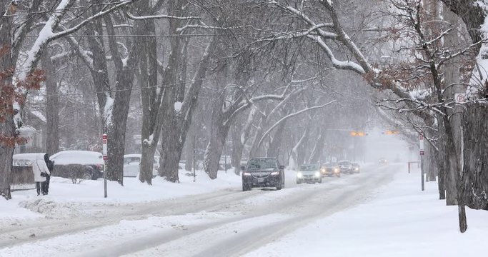 Cars drive slowly on a residential road during a winter blizzard