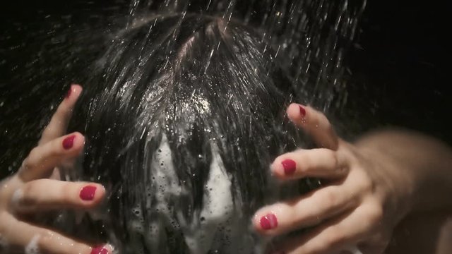 Back of Woman Head Showering Shampoo Rinse Off Slow Motion. a woman close up of the back of her head rinsing out shampoo as water streams in slow motion on black
