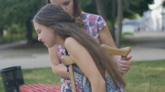 Mom helps my daughter with a broken leg on crutches to walk along the street