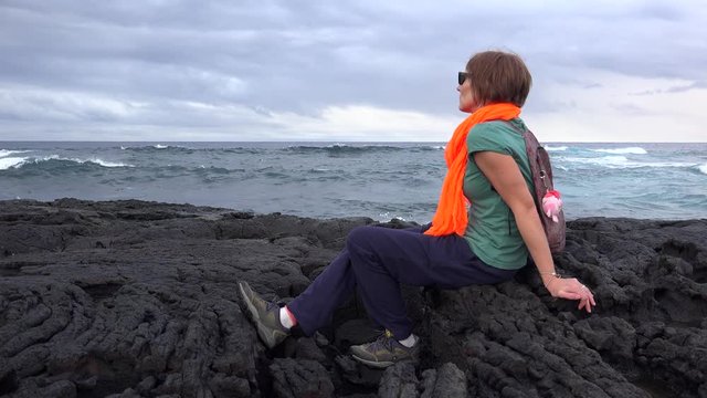 Girl looks at the ocean on Lava rocky shoreline near the Punaluu Black Sand Beach. Big Island, Hawaii, USA
