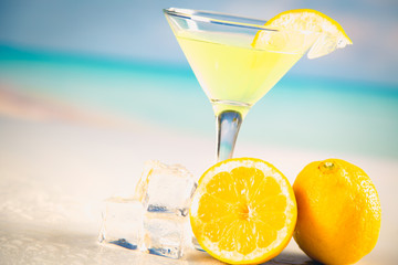 Yellow cold drink on a beach with lemon and ice