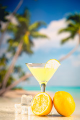 Yellow cold drink on a beach with lemon and ice