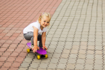 Fototapeta premium A blonde little girl is riding on a skateboard while sitting.