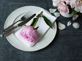 Place setting with peony flower and white napkin on the plate