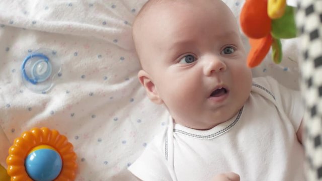 Top view shot of cute baby with soother lying in crib and looking at spinning taddy bear toys. The baby looks around and then smiles and laughs. Concept of caring for children, parental love and lack