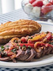 Steak topped with pepper and caper salad, with side dishes