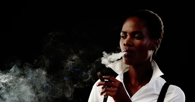 Androgynous man smoking cigar against black background