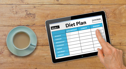 Hands with Computer Tablet completing Diet Plan App on Table with Coffee or Tea
