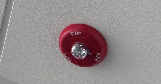 An extreme close up shot of a fire alarm warning light on the ceiling of an office, airport, or other commercial building.	