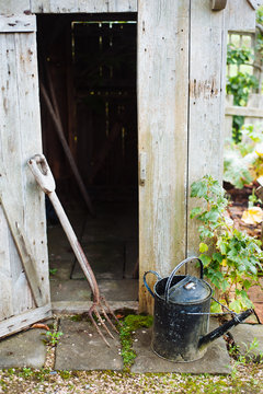 Rusty garden fork and watering can next to a garden shed