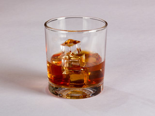 Glass of whiskey and ice on plain background