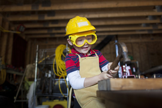 Little Boy in Garage Hammering a Nail with Hardhat and Goggles