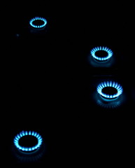 burning gas stove hob blue flames close up in the dark with inverted reflection on black background