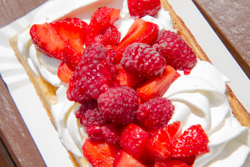 Waffle topped with whipped cream and freshly chopped strawberries and raspberries on a paper plate