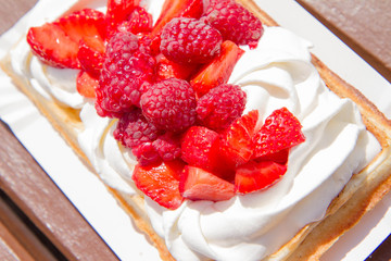 Waffle topped with whipped cream and freshly chopped strawberries and raspberries on a paper plate