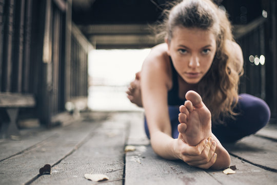 Young blonde woman doing yoga on the wooden porch. 