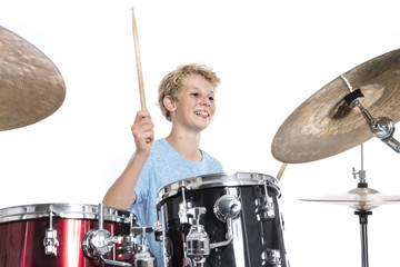blond teen boy plays drums at drumkit in studio against white background