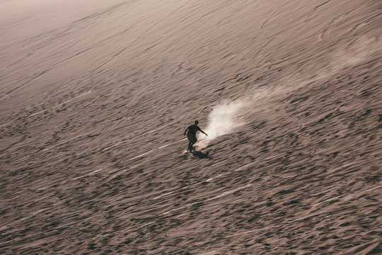 Silhouette of man doing sandboard on desert dunes