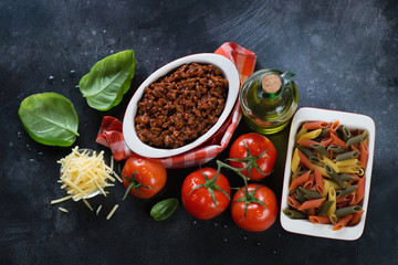 Bolognese sauce with italian traditional cooking ingredients, high angle view on a dark metal background, horizontal shot