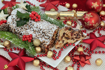 Traditional christmas chocolate stollen cake on a plate with slice, red and gold bauble decorations, foil wrapped chocolates, holy and fir.
