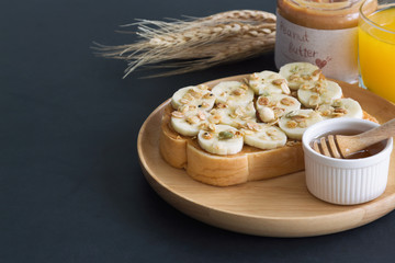 Banana peanut butter toast sandwich on wood plate with honey. Homemade open sandwich spread with peanut butter on top with banana slice and granola. Delicious healthy sandwich for breakfast or lunch.