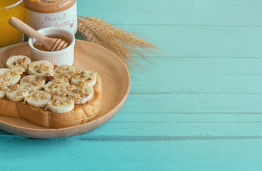 Banana peanut butter toast sandwich on wood plate with honey. Homemade open sandwich spread with peanut butter on top with banana slice and granola. Delicious healthy sandwich for breakfast or lunch.