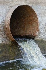 Dirty water flows out of a large rusty metal pipe