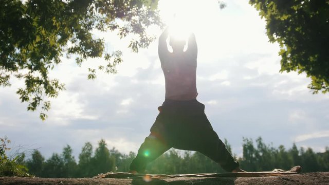 Silhouette of young sportive man instructor practicing yoga at morning sunrise