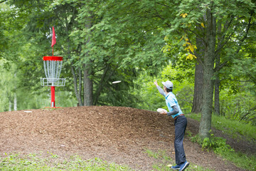 Professional disc golf athlete is throwing the disc in to the basket outdoors.