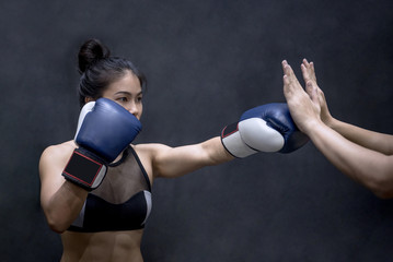 Plakat Young Asian woman boxer with blue boxing gloves punching to her trainer’s hand in training gym, Martial arts on black background