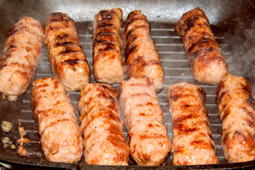 Close-up of traditional romanian barbecue raw meat (mici, mititei) on hot grill with smoke, selective focus
