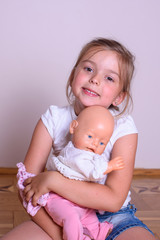 Beautiful child girl playing with a doll as mother with a newborn baby
