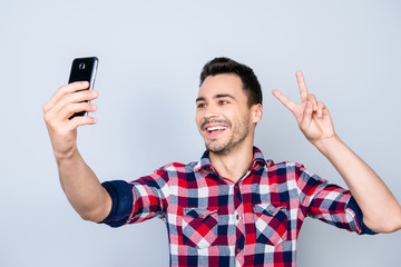 Selfie time! Young funky blogger is making photo for his social networks page, he is posing in a casual outfit and gesturing peace sign
