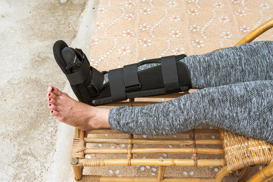 injury woman with black splint on leg  sitting on wooden chair at home, Travel insurance concept.