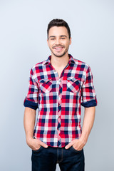Fototapeta premium Success concept. Smiling young stylish bearded brunet student in bright casual checkered shirt is standing on light background