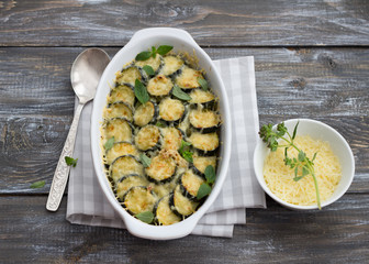 Gratin zucchini with cheese and greens on a wooden background. Delicious homemade food