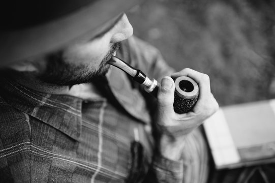 man in hat and flannel smoking a tobacco pipe