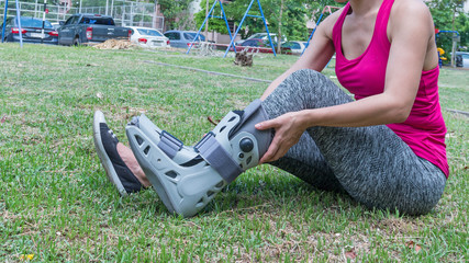 injured woman wearing sportswear  broken ankle wearing ankle support on exercise equipment in a public park background, health care concept